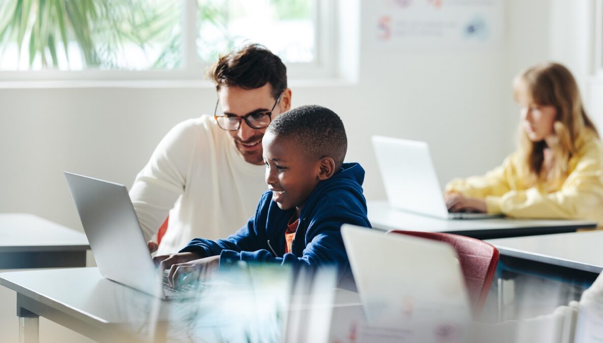 Un enseignant aide un jeune garçon à apprendre l'informatique en classe. Un tuteur donne un cours dans une école primaire, axé sur le codage et les bases de la culture numérique.
