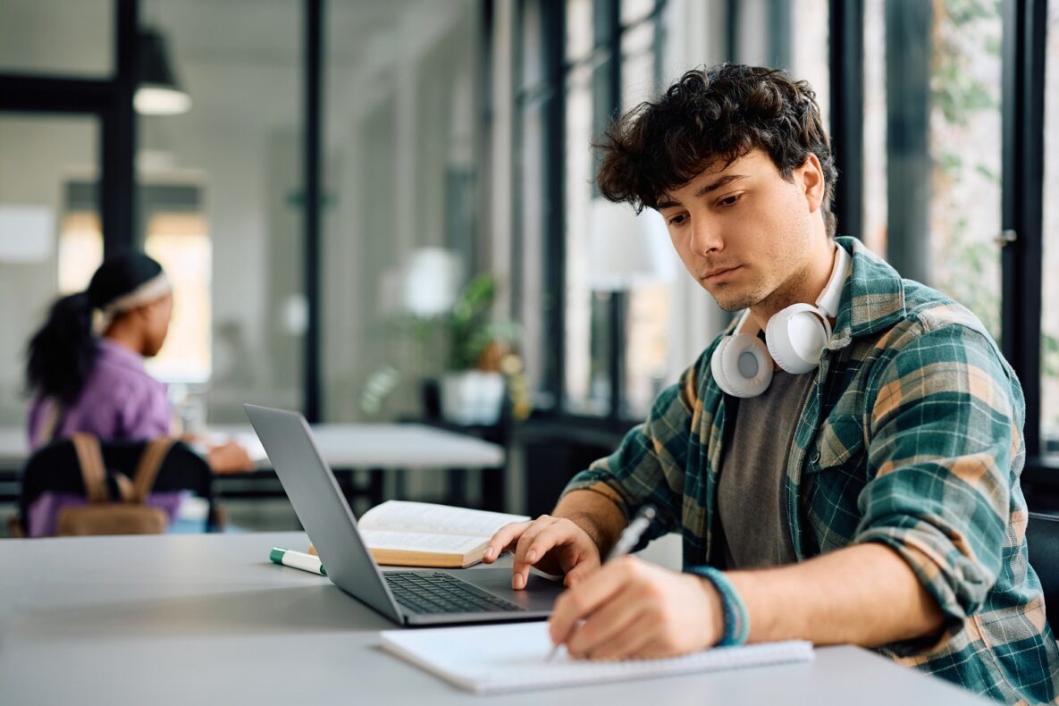 Un étudiant universitaire écrit tout en utilisant un ordinateur portable et en étudiant en classe.