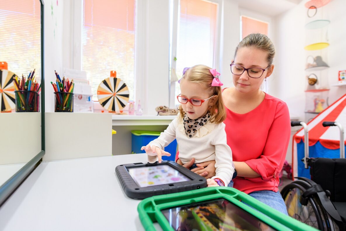 Jeune fille non verbale atteinte de paralysie cérébrale, apprenant à utiliser une tablette numérique pour communiquer.