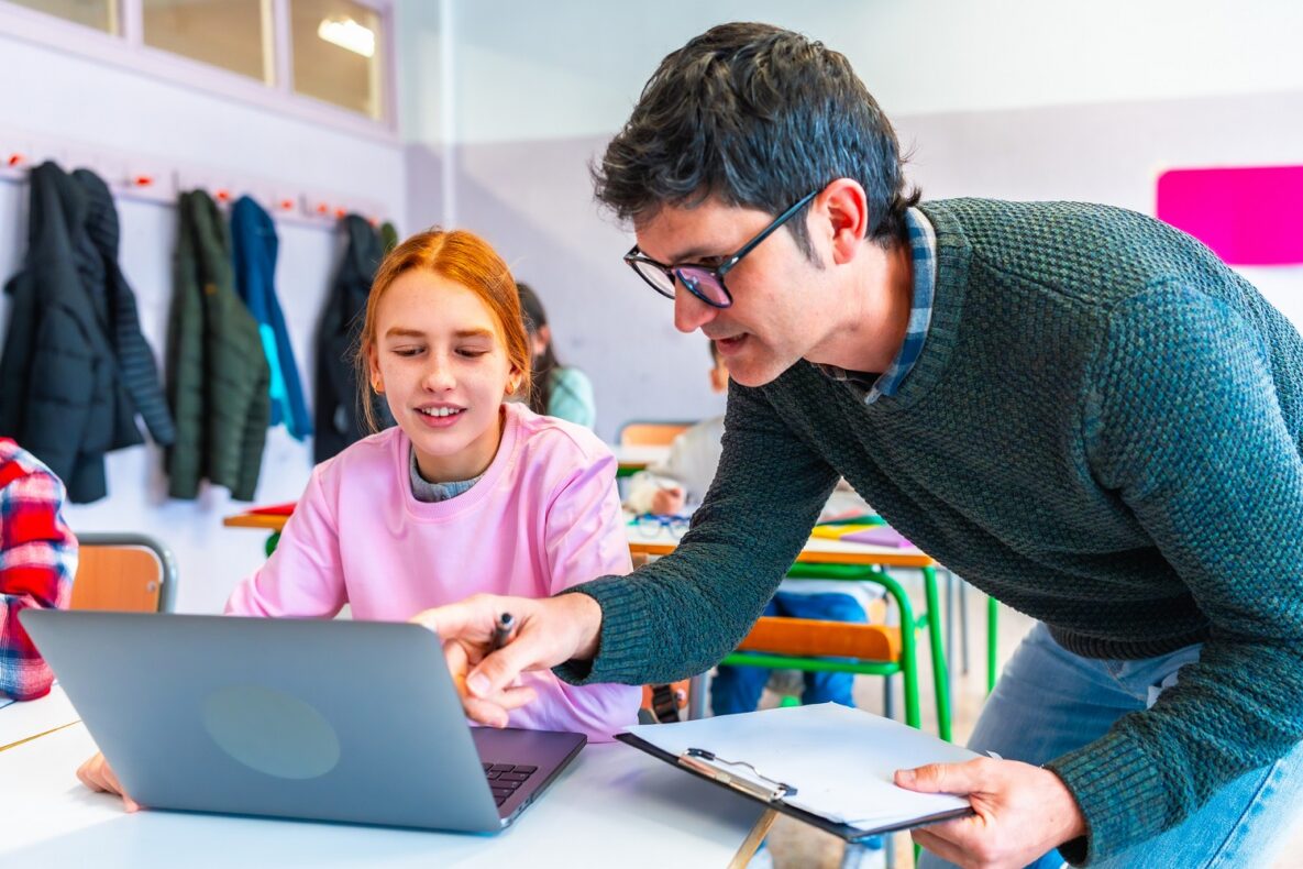 Un professeur aide une élève à utiliser un ordinateur portable pendant le cours.