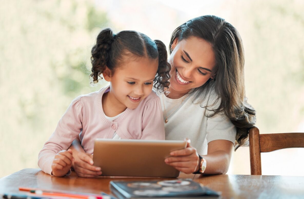 Une mère souriante fait l'école à la maison à sa fille avec une tablette numérique.